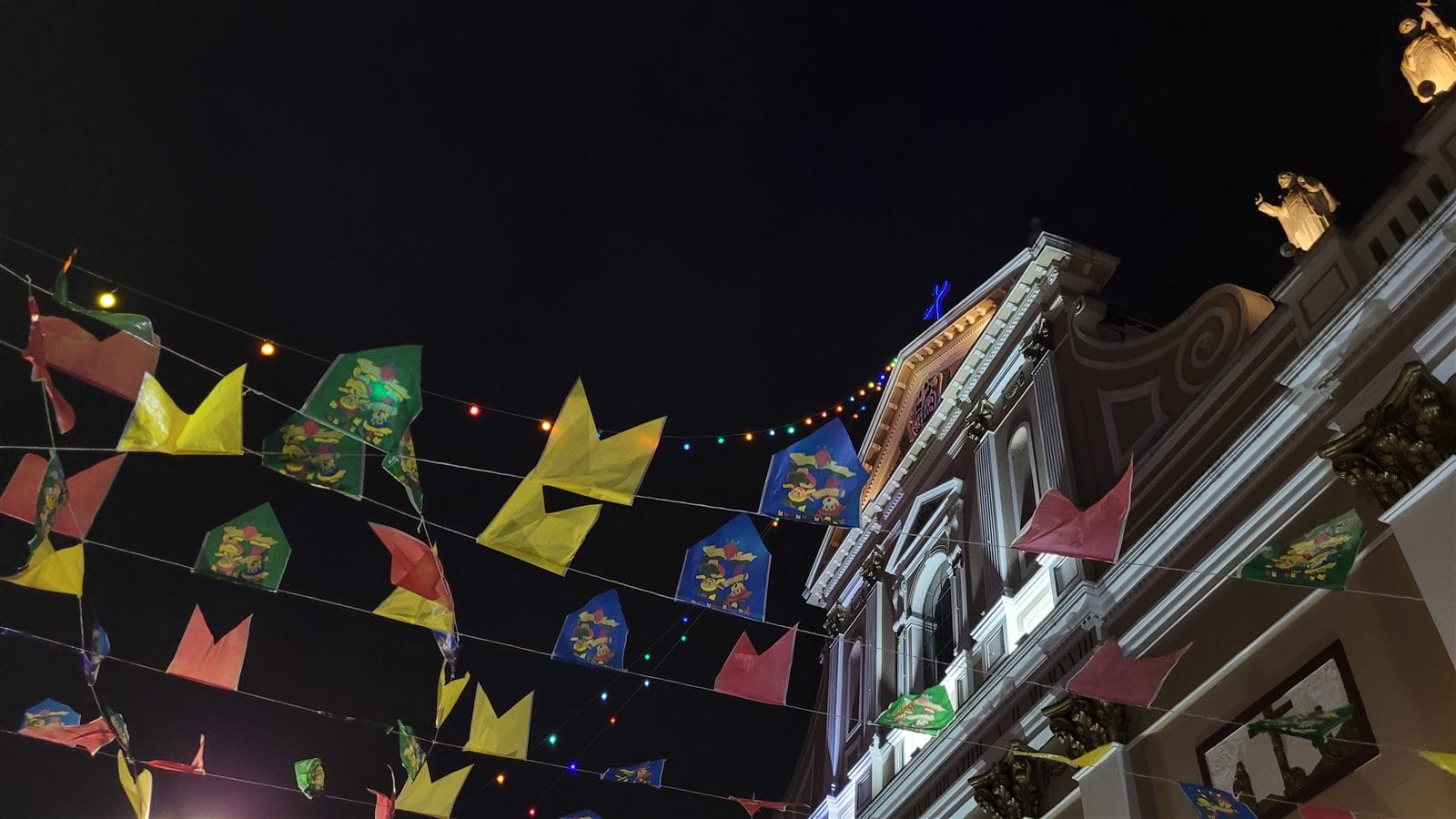 Mesas e barracas de quermesse de igreja em festa junina, com bandeirinhas iluminadas no alto