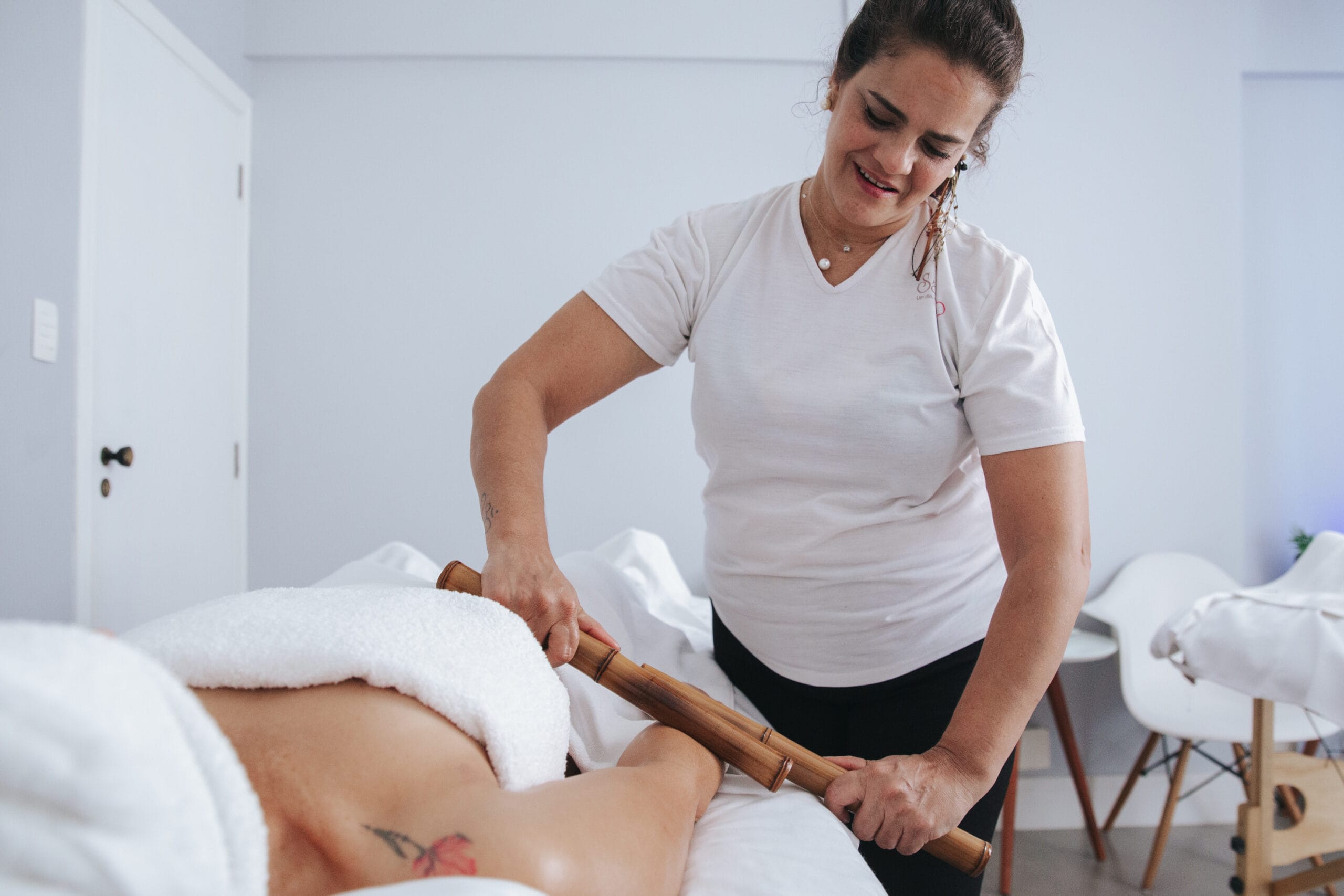 Profissional da Sala Vip Spa aplicando massagem com bastões de bambu nas pernas de uma cliente.
