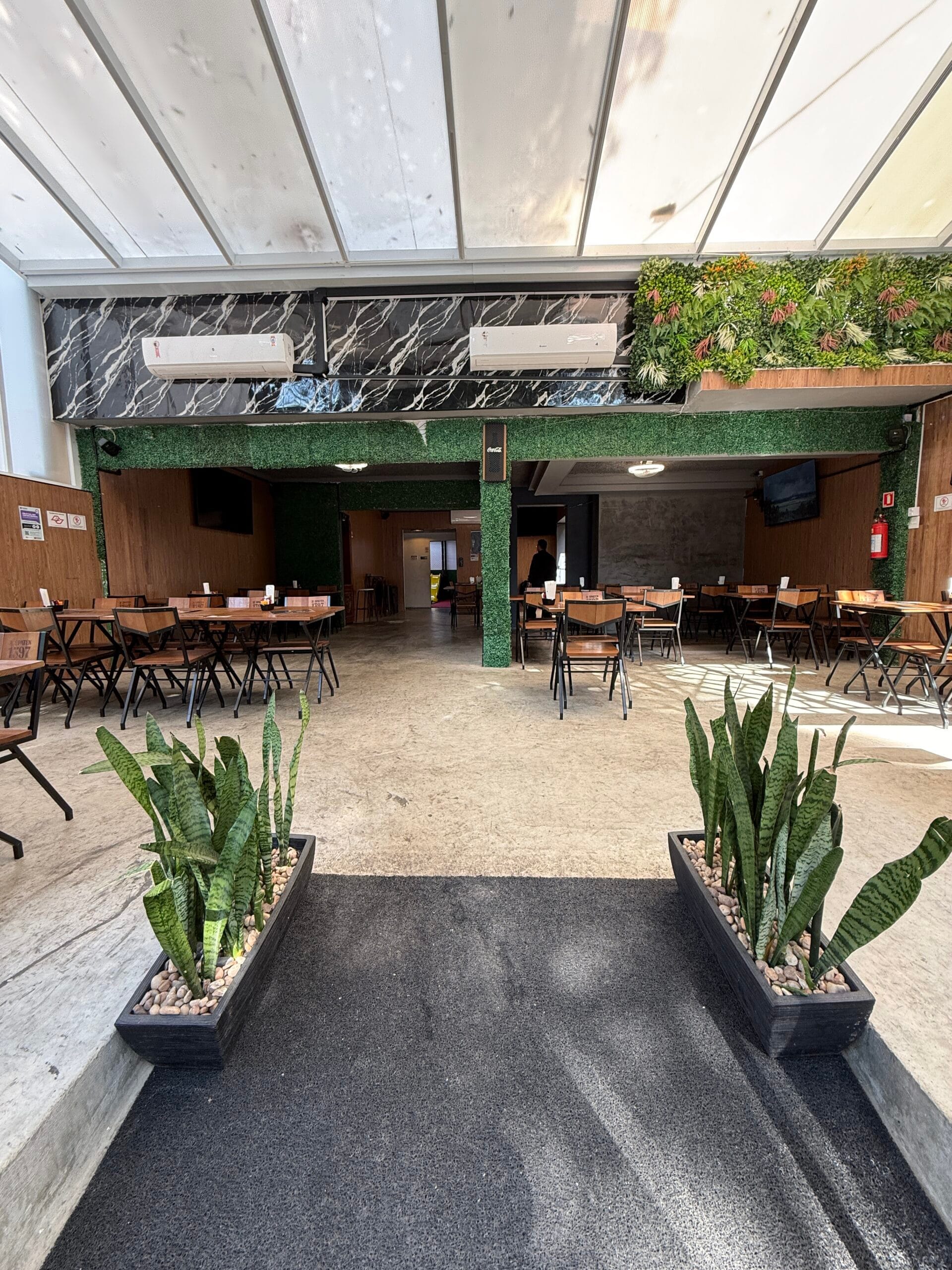 Entrada do Zora Bar com jardim vertical, plantas e tapete preto, em Santos