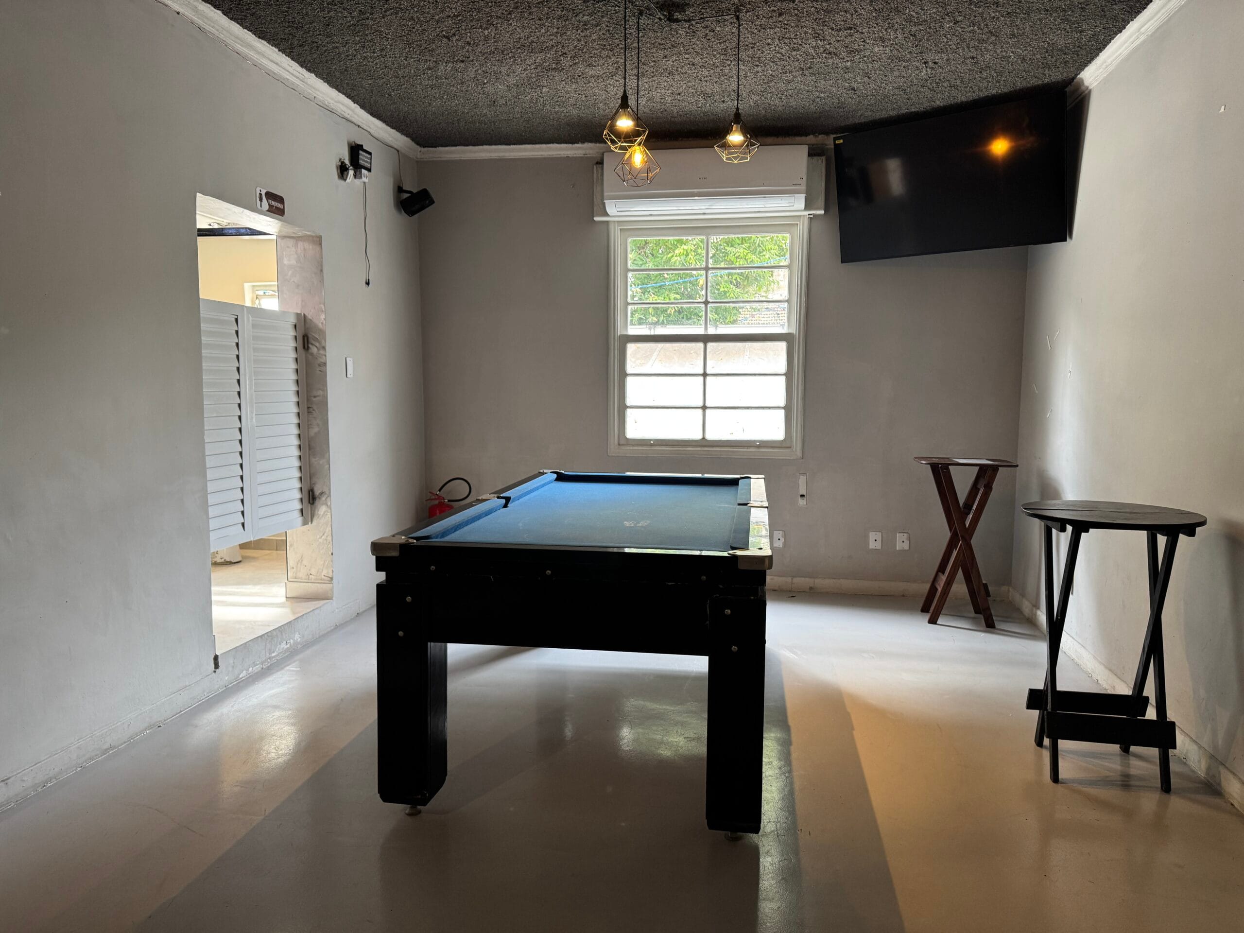 Sala de sinuca do Zora Bar com mesa azul, ar-condicionado e TV