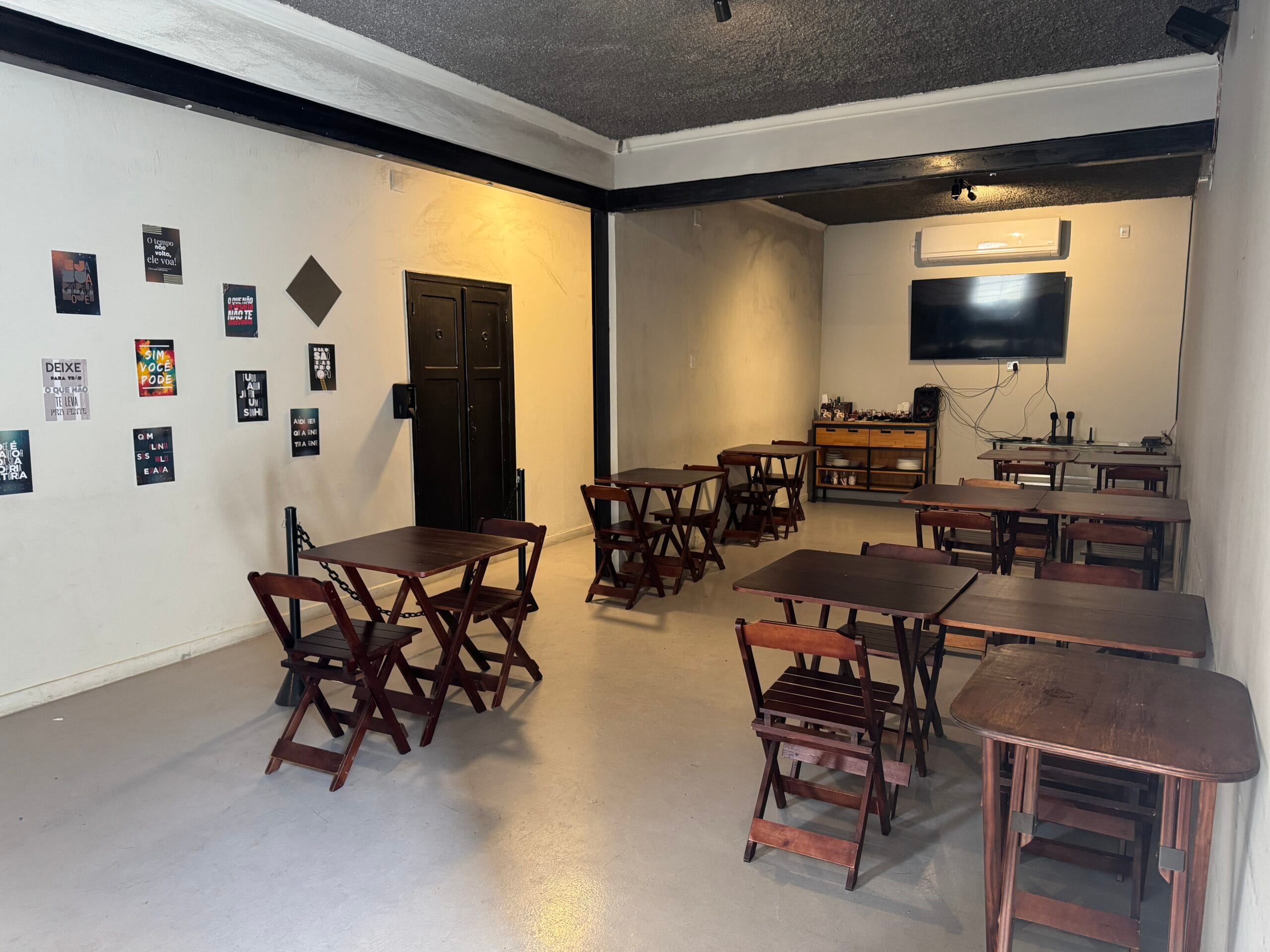 Salão interno do Zora Bar com mesas de madeira e parede com posters motivacionais