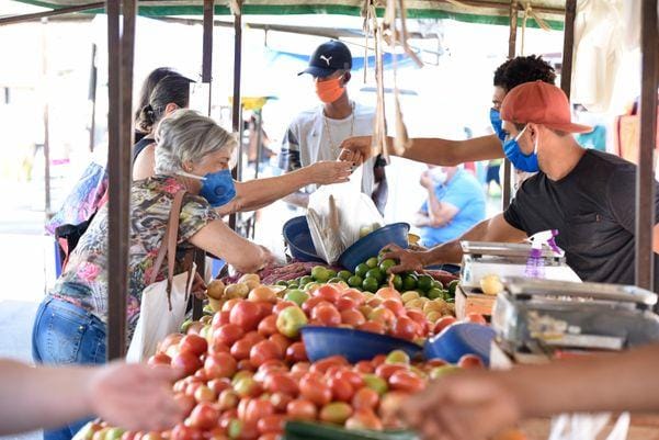 Banca de tomates e limões em feira livre de Santos, com feirantes e fregueses em volta