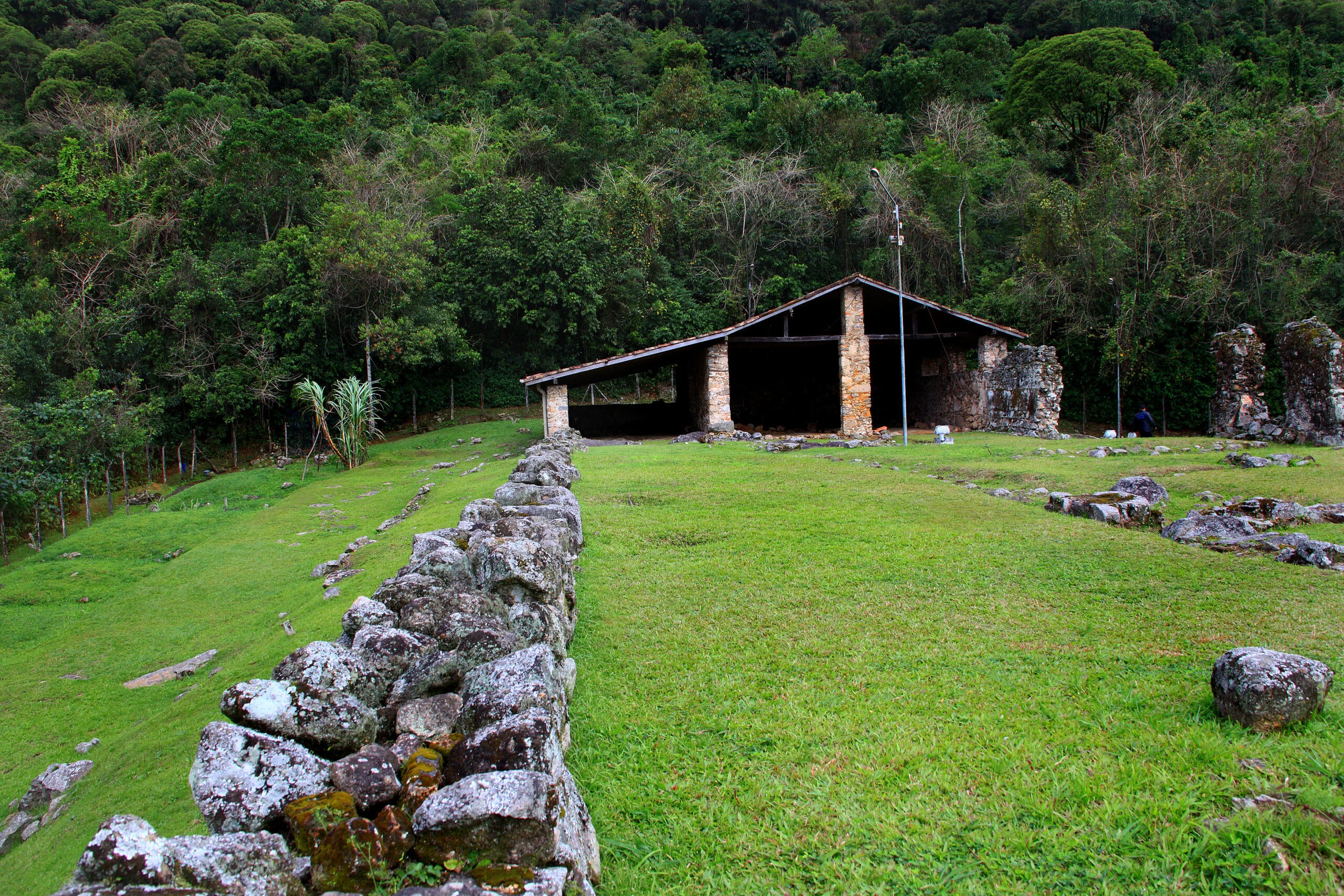 Ruínas do Engenho São Jorge dos Erasmos, com muros de pedra e cobertura de proteção, no sopé do Morro da Caneleira, em Santos.