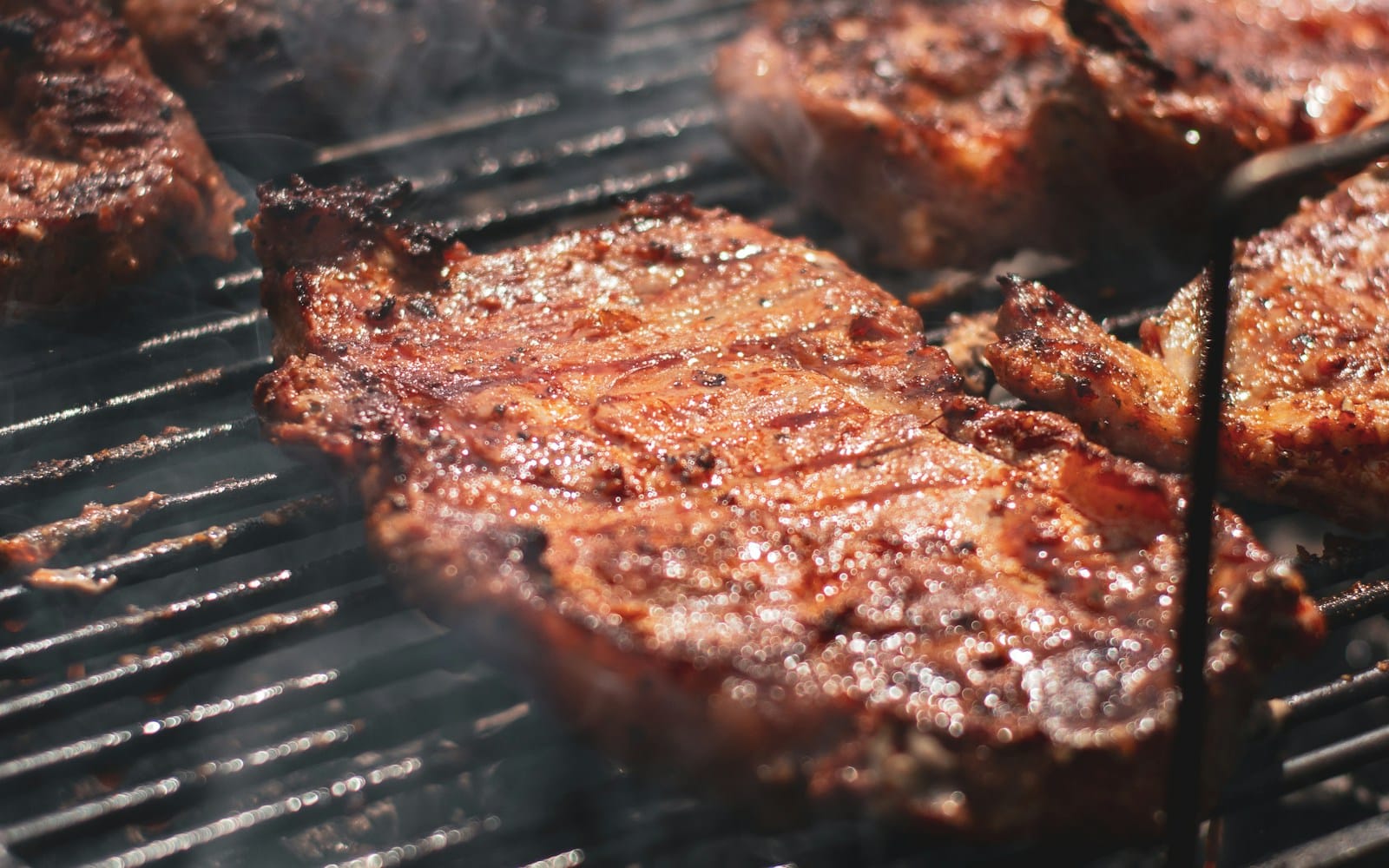 Peças de carne assando na grelha sobre brasa, com fumaça, em churrascaria.